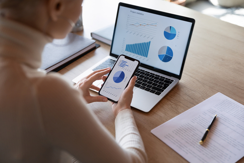 Woman checking charts on phone and laptop